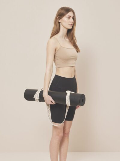 Yogi with her yoga mat, dressed in a beige yoga tank top and tight black biker shorts