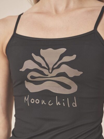 Woman wearing a black sports tank top with thin straps, a moonflower design, and Moonchild brand on the front