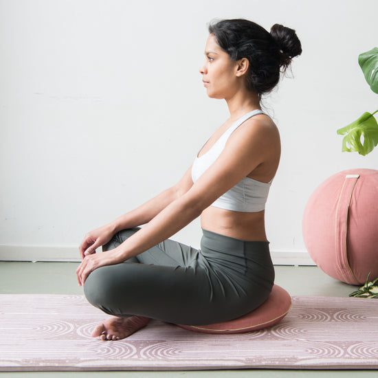 Woman meditating seated on a pink cushion