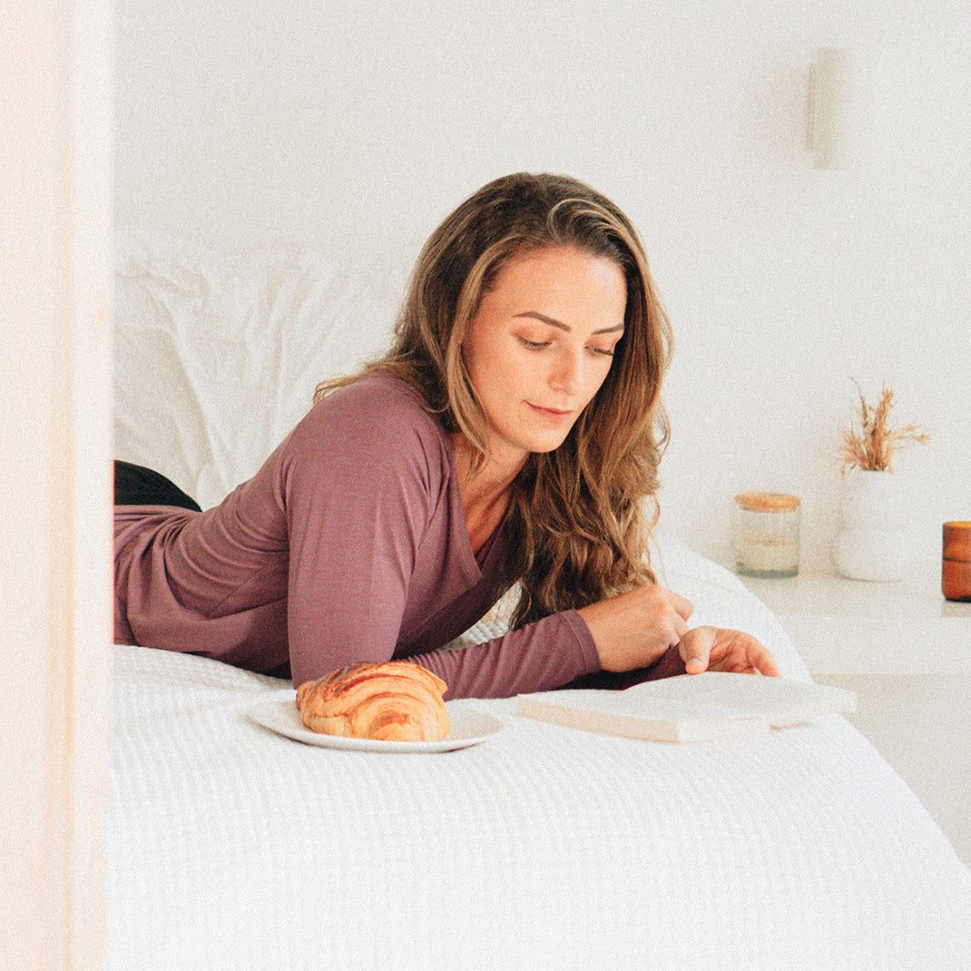 Woman lying down reading, wearing an aubergine long sleeve t-shirt top with a slight V-neck.