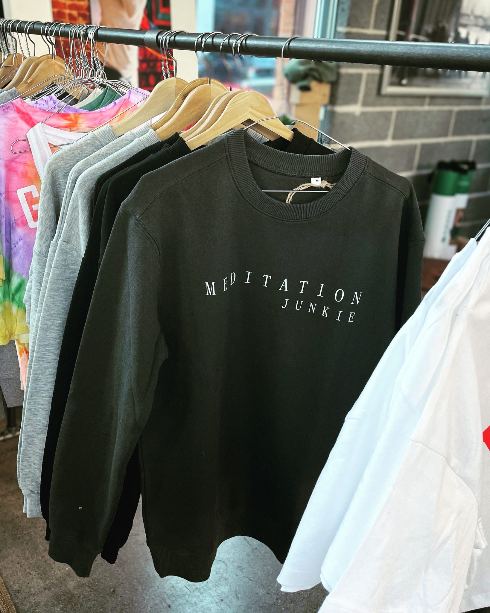 Dark grey sweatshirt with "Meditation Junkie" in white on the chest, hanging on a hanger.
