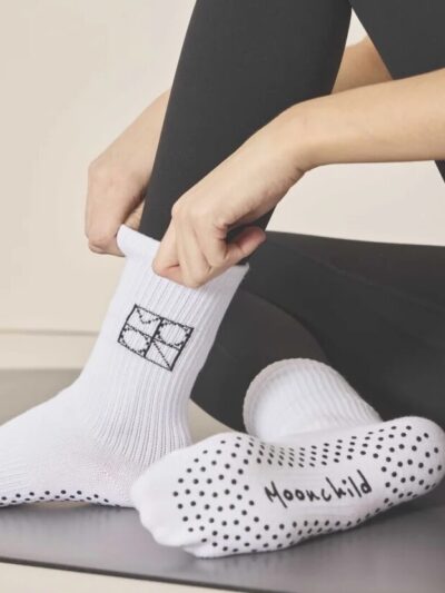 Woman putting on white grip Pilates socks with black grip dots on the sole and Moonchild logo.