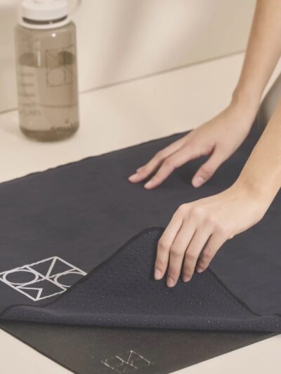 Black yoga towel with white Moonchild logo placed on a black yoga mat with a water bottle