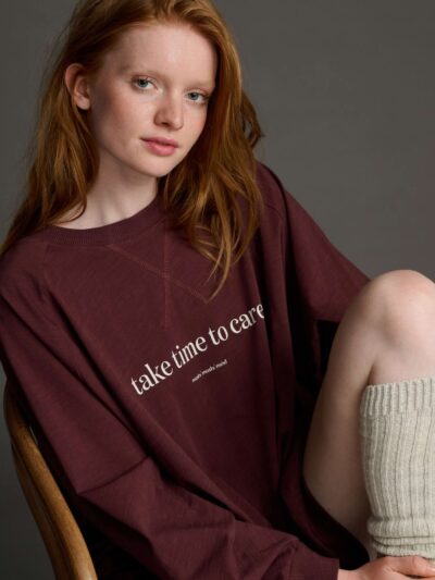 A woman with long red hair wearing a burgundy sweatshirt with white lettering on the front